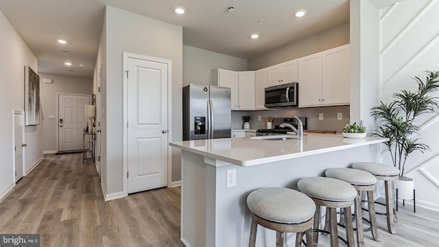 kitchen featuring kitchen peninsula, a kitchen breakfast bar, stainless steel appliances, white cabinets, and light hardwood / wood-style floors