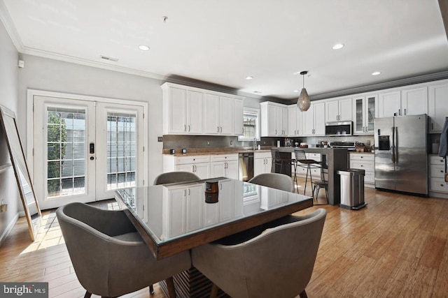 dining space featuring light wood-type flooring, french doors, crown molding, and sink