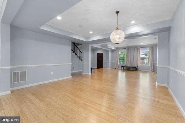 unfurnished living room featuring light hardwood / wood-style floors, an inviting chandelier, ornamental molding, and a tray ceiling