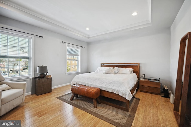 bedroom with multiple windows, light wood-type flooring, and a raised ceiling