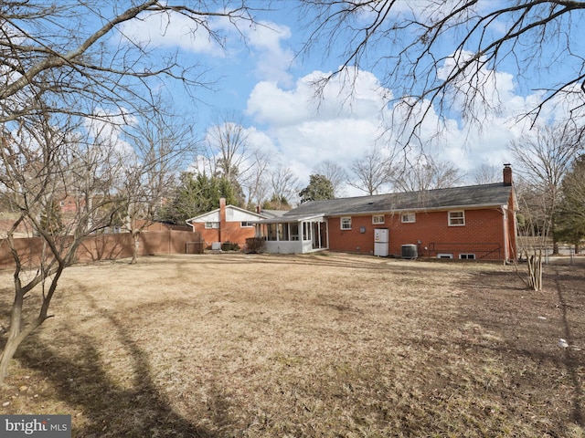 rear view of house featuring a sunroom, central AC unit, and a lawn