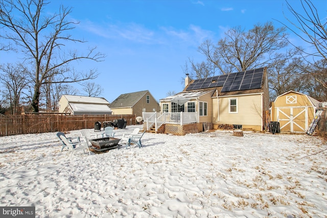 snow covered rear of property featuring a deck, a shed, solar panels, and a fire pit