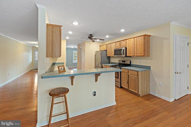 kitchen featuring light hardwood / wood-style flooring, stainless steel appliances, a kitchen breakfast bar, kitchen peninsula, and light brown cabinets