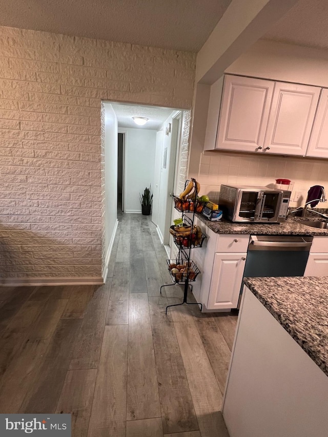 kitchen featuring white cabinets, a textured ceiling, dark stone countertops, stainless steel dishwasher, and wood-type flooring