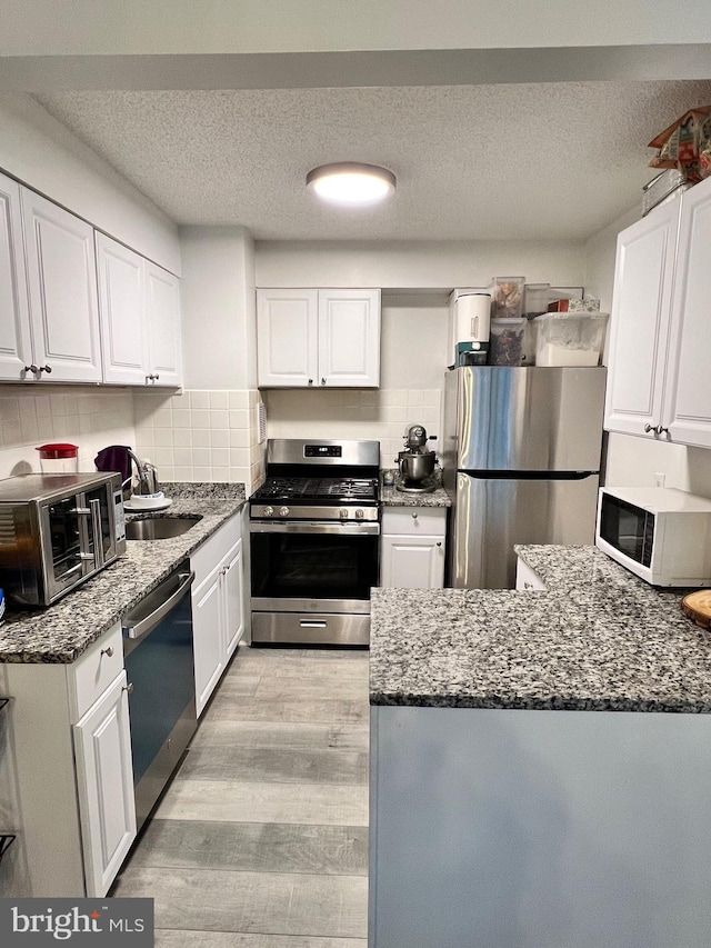 kitchen featuring stainless steel appliances, sink, white cabinetry, light hardwood / wood-style floors, and backsplash