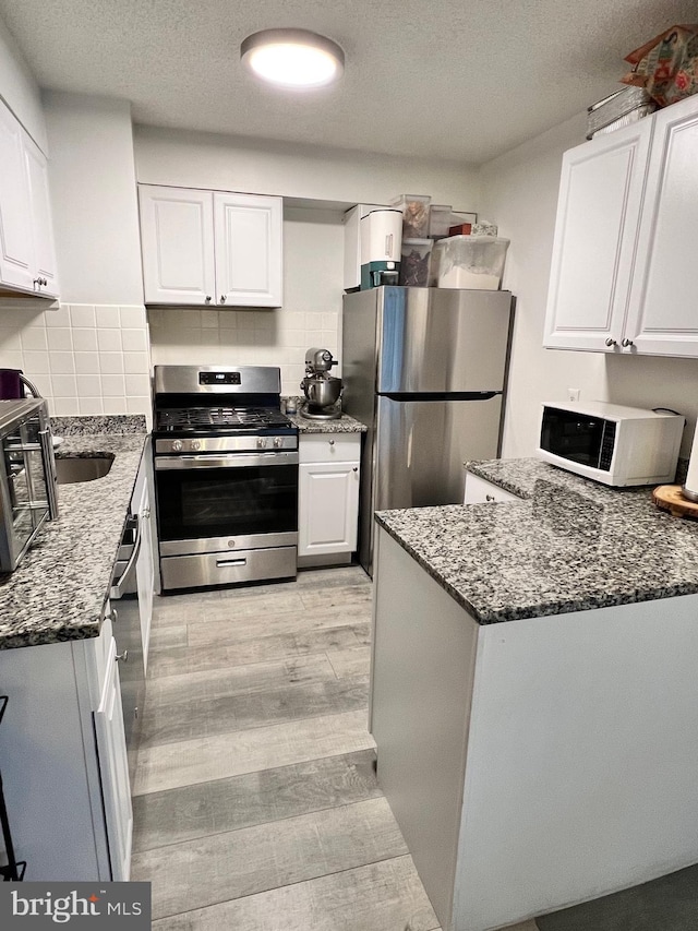 kitchen with white cabinets, dark stone countertops, light hardwood / wood-style floors, tasteful backsplash, and appliances with stainless steel finishes