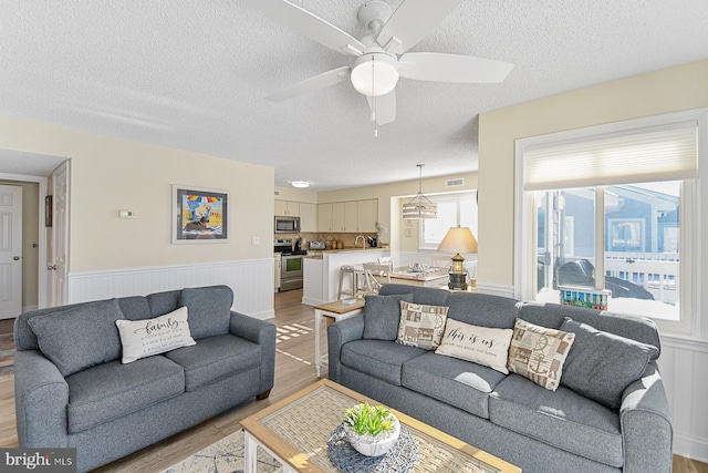 living room featuring a textured ceiling, light wood-type flooring, and ceiling fan