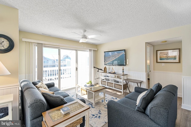 living room featuring ceiling fan, light hardwood / wood-style flooring, and a textured ceiling