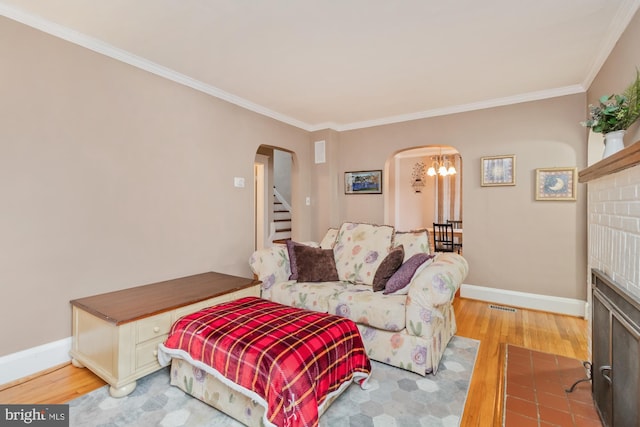 living room featuring light wood-type flooring, ornamental molding, a chandelier, and a fireplace