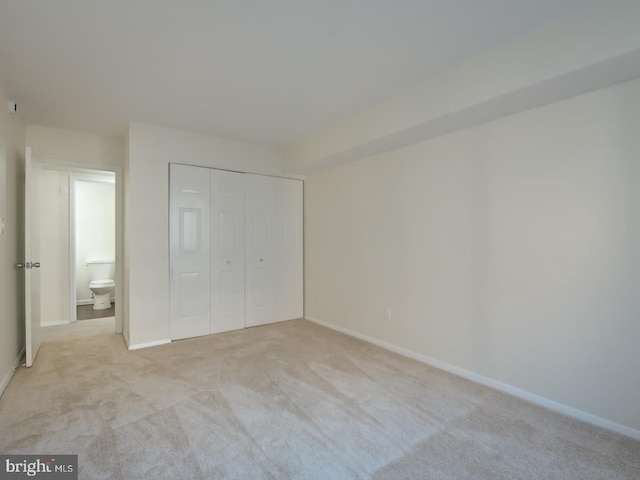 unfurnished bedroom featuring light carpet, connected bathroom, and a closet