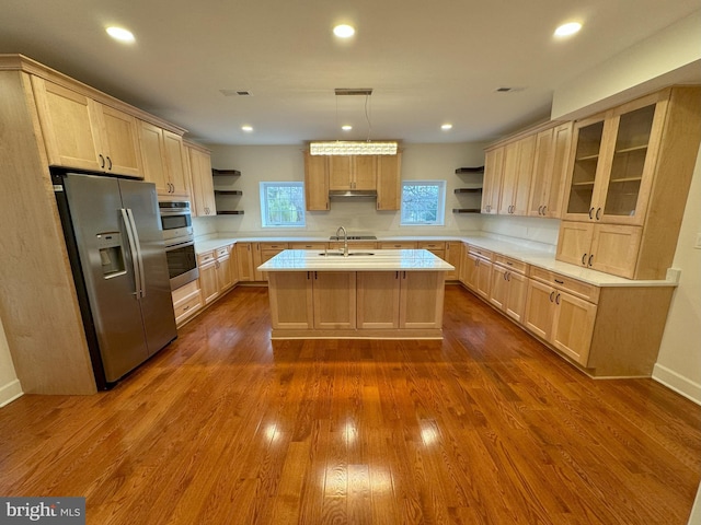 kitchen with sink, hanging light fixtures, light brown cabinets, stainless steel appliances, and a kitchen island with sink