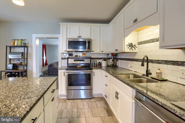 kitchen featuring tasteful backsplash, white cabinets, appliances with stainless steel finishes, and a sink