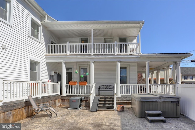 view of exterior entry with a patio, a balcony, cooling unit, a porch, and a hot tub