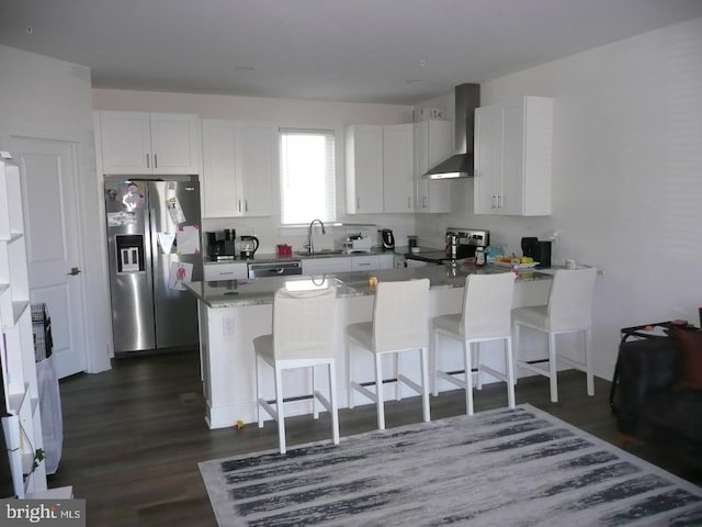 kitchen featuring a breakfast bar, sink, wall chimney exhaust hood, appliances with stainless steel finishes, and white cabinetry