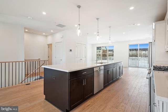 kitchen featuring appliances with stainless steel finishes, white cabinetry, an island with sink, hanging light fixtures, and light hardwood / wood-style flooring