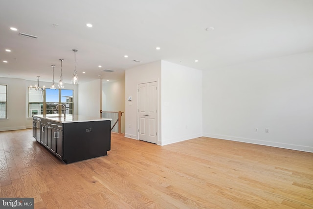 kitchen with hanging light fixtures, a kitchen island with sink, sink, and light hardwood / wood-style flooring