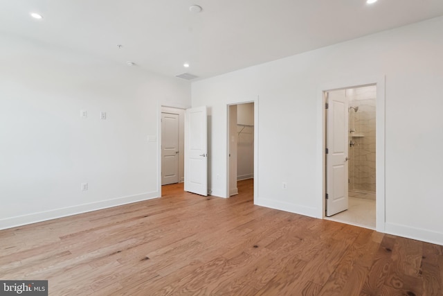 unfurnished bedroom featuring a spacious closet, connected bathroom, a closet, and light wood-type flooring