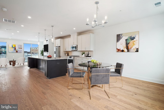 dining space with sink, light hardwood / wood-style flooring, and a notable chandelier