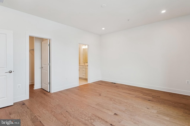 unfurnished bedroom featuring a closet, ensuite bathroom, light hardwood / wood-style flooring, and a walk in closet