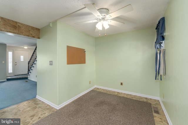 empty room featuring light colored carpet, visible vents, a textured ceiling, baseboards, and stairs