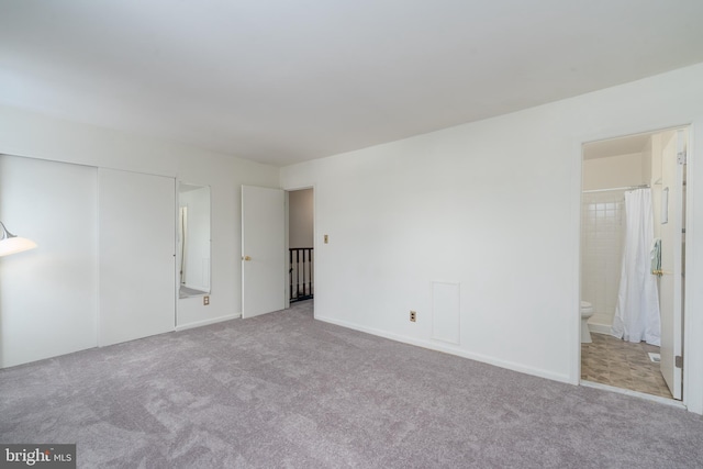 unfurnished bedroom featuring ensuite bathroom, a closet, baseboards, and light colored carpet