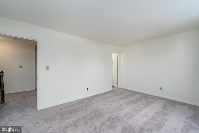 empty room featuring light carpet, attic access, and baseboards