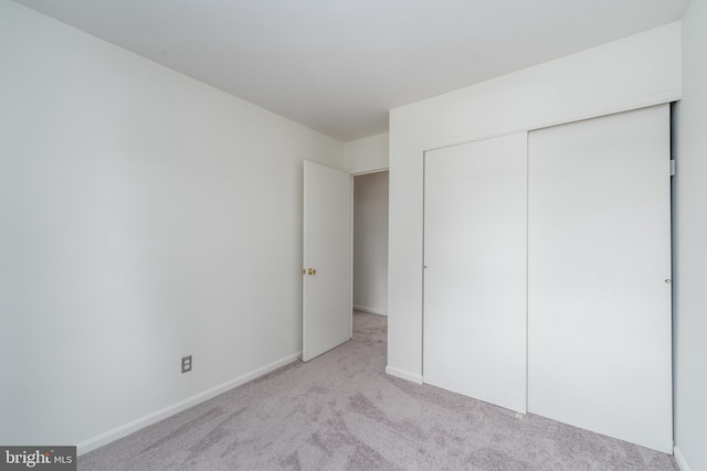 unfurnished bedroom featuring light carpet, baseboards, and a closet