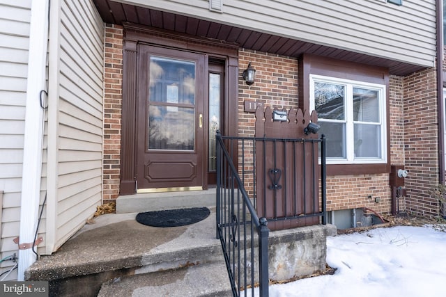 snow covered property entrance with brick siding