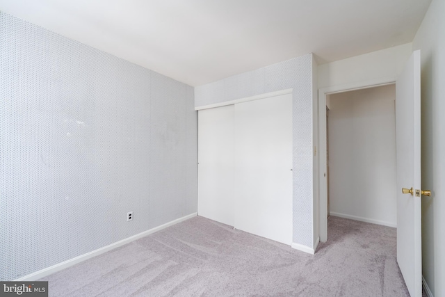 unfurnished bedroom with light carpet, baseboards, and a closet