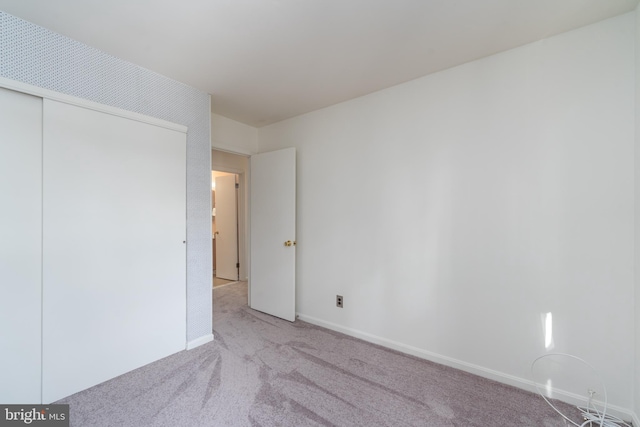 unfurnished bedroom featuring light carpet, a closet, and baseboards