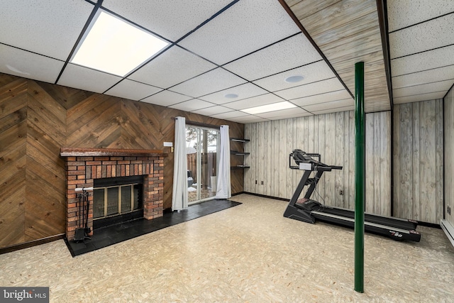 exercise room featuring a drop ceiling, wood walls, a fireplace, and baseboards