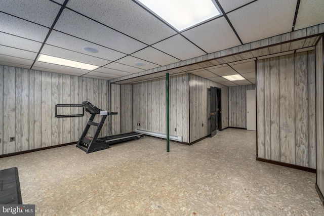 workout area with wooden walls, baseboard heating, a paneled ceiling, and baseboards