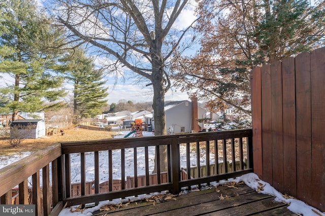 snow covered deck featuring a playground, a storage shed, an outdoor structure, fence, and a residential view