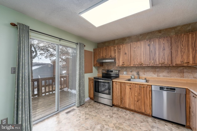 kitchen featuring stainless steel appliances, visible vents, light countertops, a sink, and under cabinet range hood