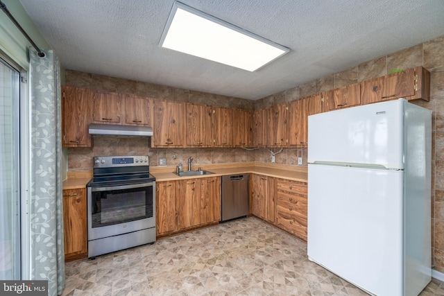 kitchen with brown cabinetry, appliances with stainless steel finishes, light countertops, under cabinet range hood, and a sink