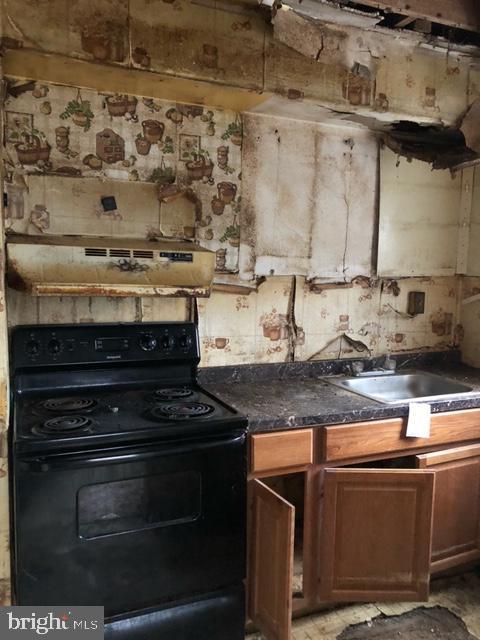 kitchen featuring black / electric stove, sink, and a wood stove