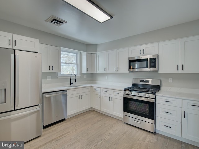 kitchen featuring appliances with stainless steel finishes, light hardwood / wood-style flooring, white cabinets, and sink