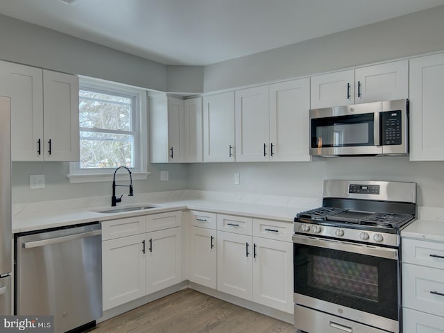 kitchen with appliances with stainless steel finishes, light hardwood / wood-style floors, light stone counters, sink, and white cabinetry