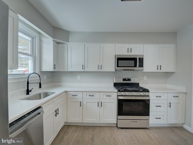 kitchen with appliances with stainless steel finishes, white cabinetry, light hardwood / wood-style flooring, and sink