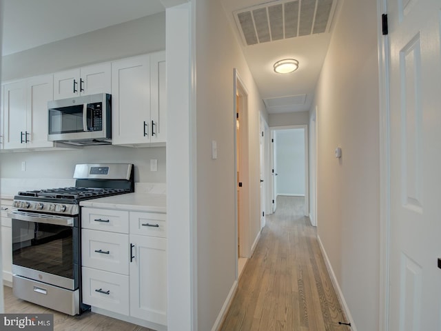 kitchen with white cabinets, light wood-type flooring, and appliances with stainless steel finishes