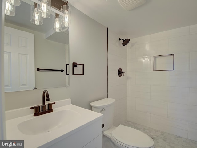 bathroom with toilet, a tile shower, and vanity