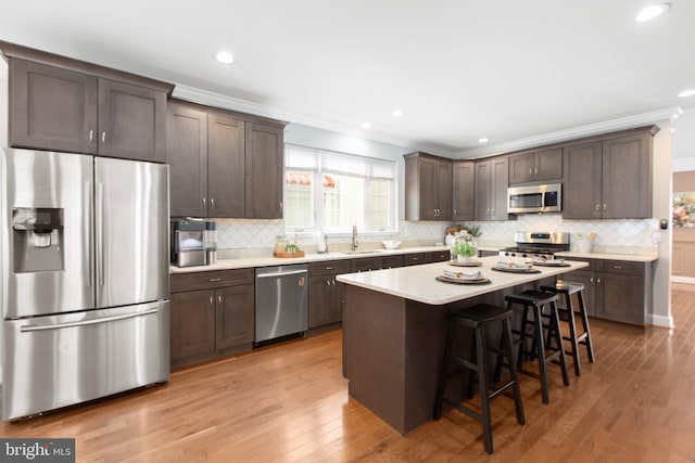 kitchen with a kitchen island, sink, a kitchen breakfast bar, stainless steel appliances, and light wood-type flooring