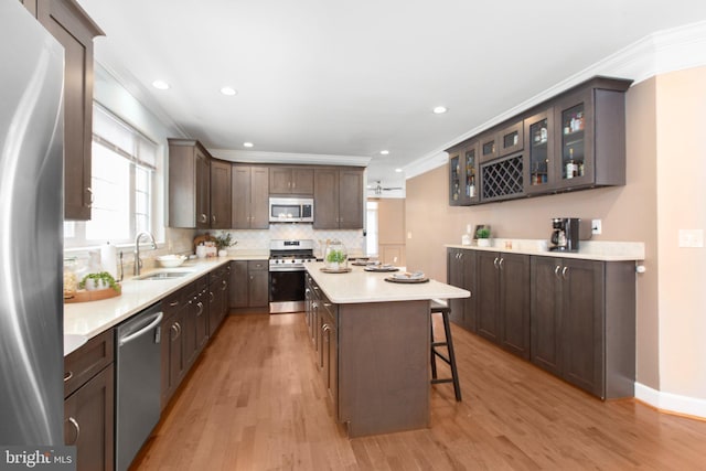 kitchen with sink, light hardwood / wood-style flooring, appliances with stainless steel finishes, dark brown cabinets, and a center island