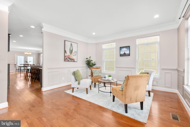 living area featuring crown molding, a chandelier, and light hardwood / wood-style flooring