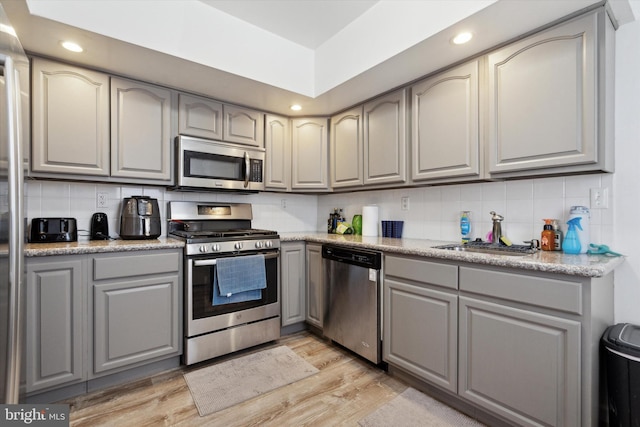 kitchen with stainless steel appliances, sink, light hardwood / wood-style floors, decorative backsplash, and gray cabinetry