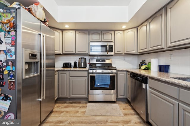 kitchen featuring decorative backsplash, light wood-type flooring, gray cabinetry, and appliances with stainless steel finishes