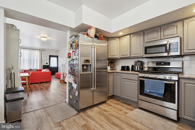 kitchen featuring appliances with stainless steel finishes, gray cabinetry, light wood-type flooring, light stone counters, and backsplash