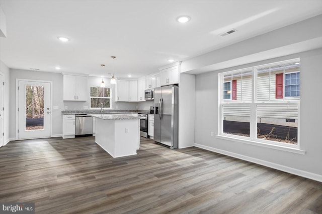 kitchen with stainless steel appliances, a center island, wood-type flooring, white cabinets, and decorative light fixtures