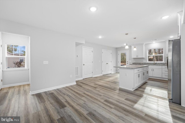 kitchen featuring light stone counters, stainless steel refrigerator, a kitchen island, pendant lighting, and white cabinets