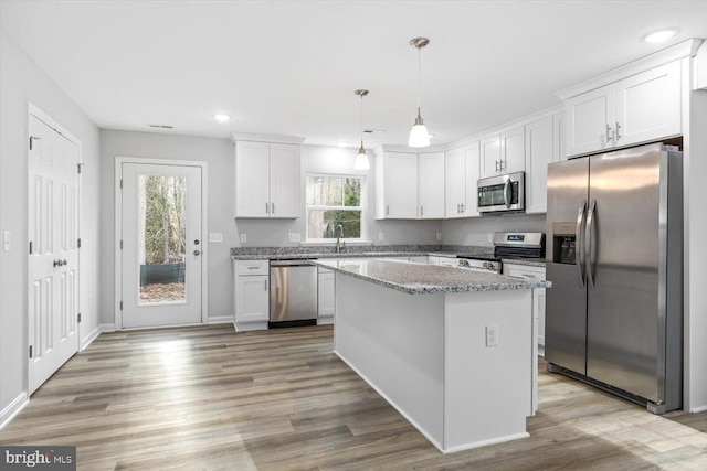 kitchen with pendant lighting, appliances with stainless steel finishes, a kitchen island, and white cabinets